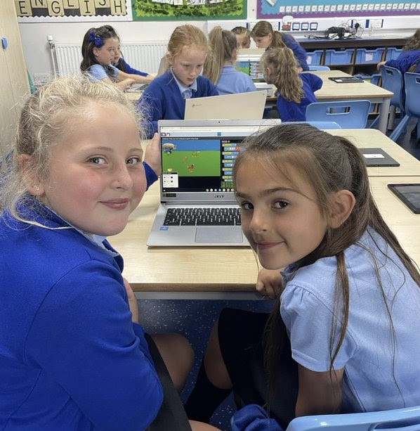 Two primary school children smiling, with their work presented on a laptop in the background.